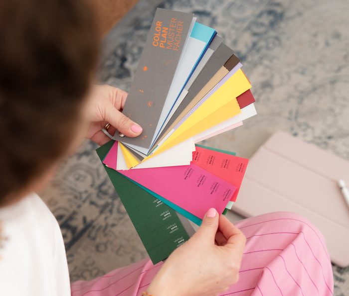 Aufgefächerte Papiermuster in Grün, Pink, Gelb und Grau in Kristinas Händen.